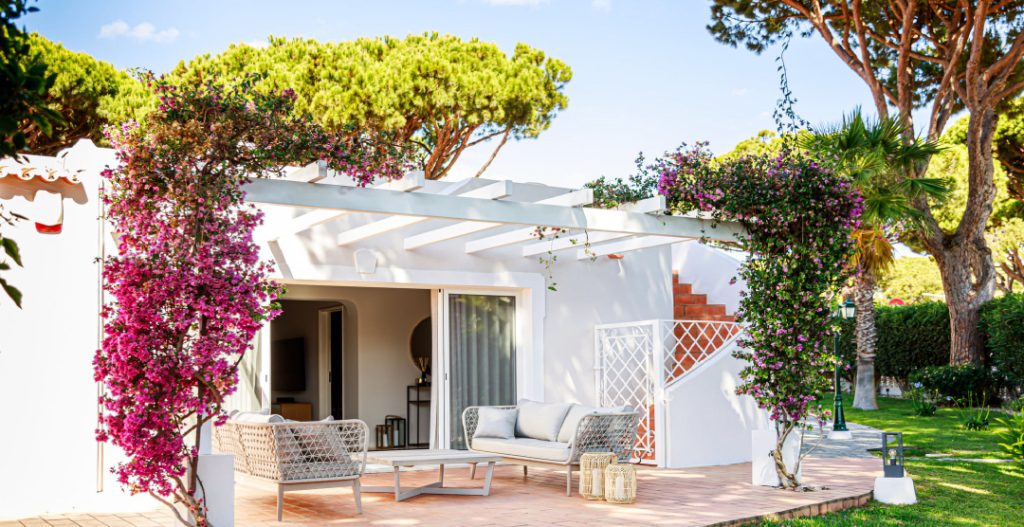 Exterior pergola setting with bespoke luxury outdoor furniture, woven detail, rattan lighting and purple bougan villa florals