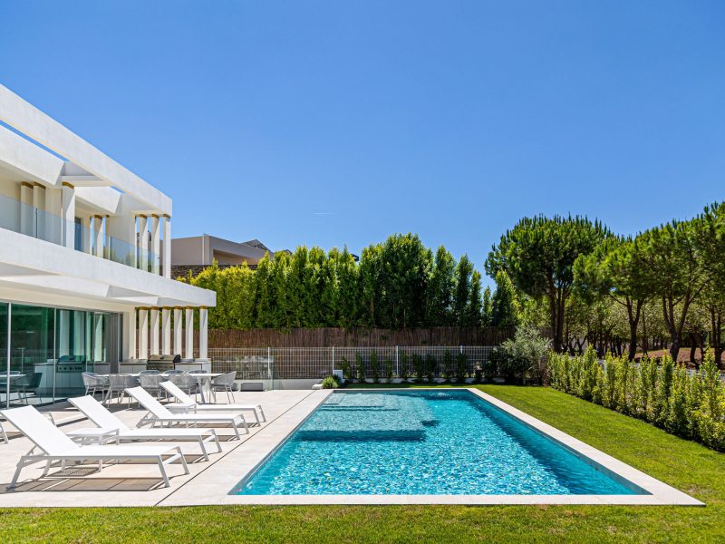 Outdoor shot of modern white luxury villa with minimalist sun loungers and clear blue skies