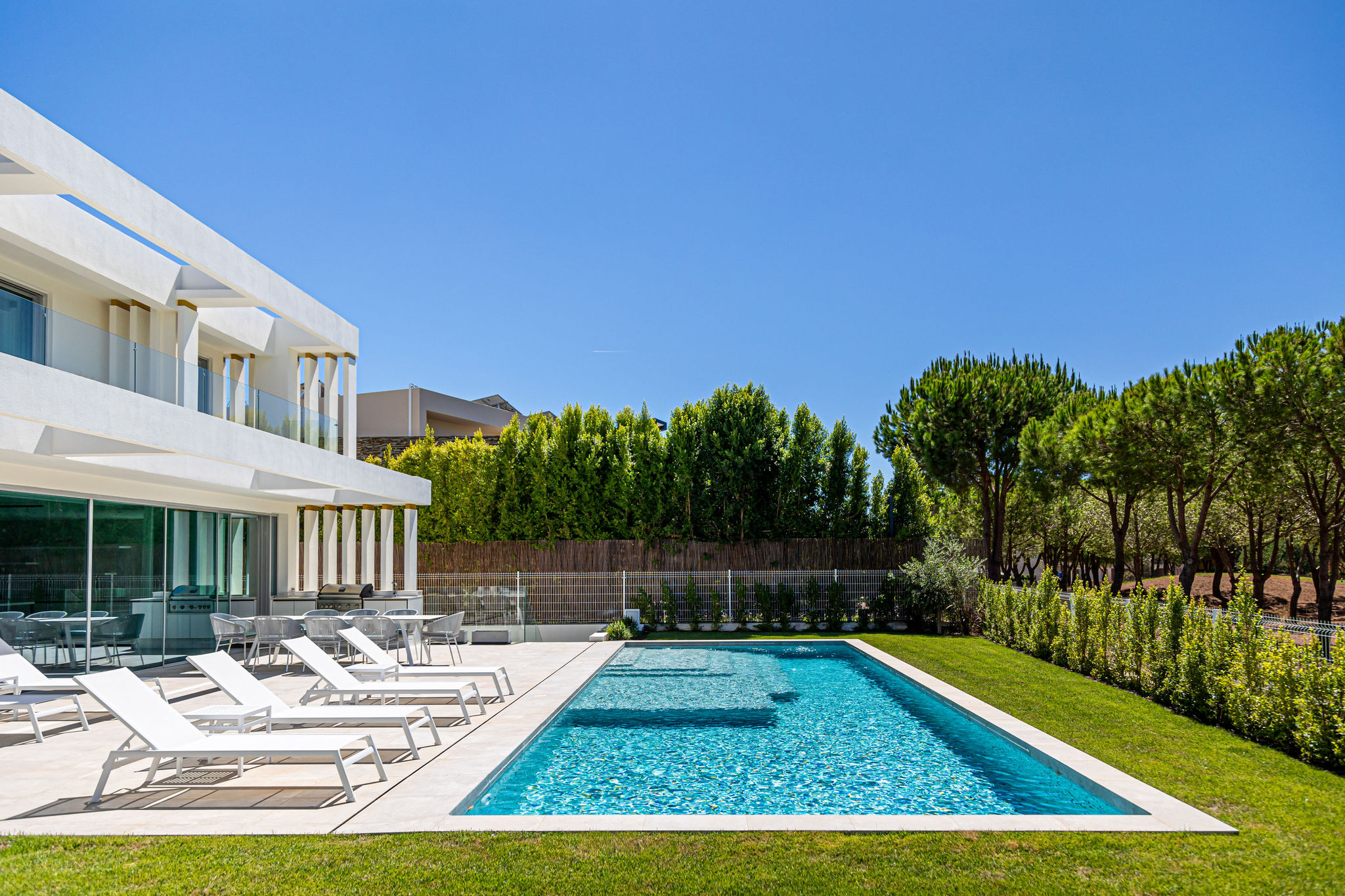 Outdoor shot of modern white luxury villa with minimalist sun loungers and clear blue skies